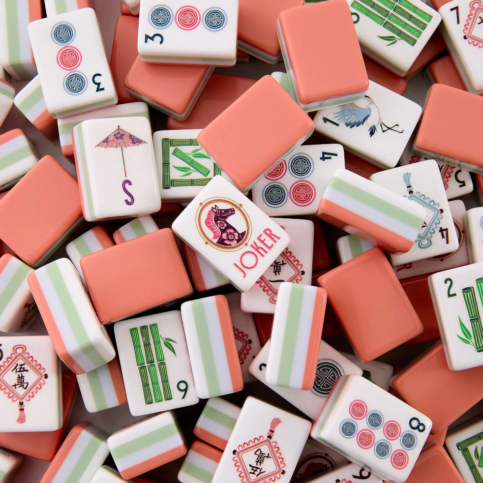 A pile of miniature Mahjong tiles in coral pink, white, and light green, featuring traditional Chinese game designs and symbols.