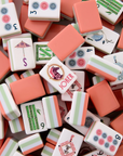 A pile of miniature Mahjong tiles in coral pink, white, and light green, featuring traditional Chinese game designs and symbols.