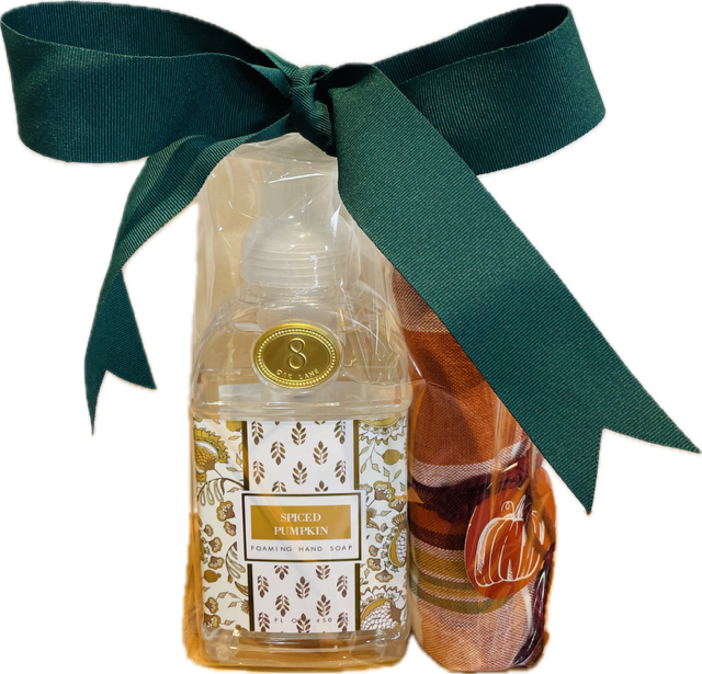 A bundled gift set containing a clear plastic-wrapped spiced pumpkin hand soap and a fall colored hand towel. 