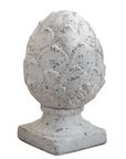 A decorative white faux-stone pinecone garden ornament with a textured, speckled finish, displayed on a wooden surface with a blurred background.