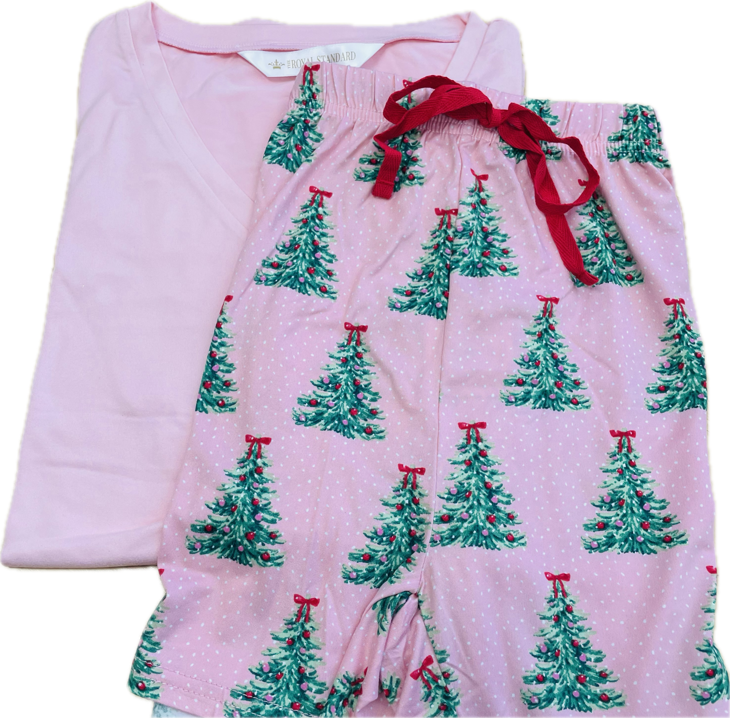 A folded pair of pink pajama shorts with an all-over green Christmas tree print and red drawstring waist, shown next to a matching solid pink folded shirt on a white background.