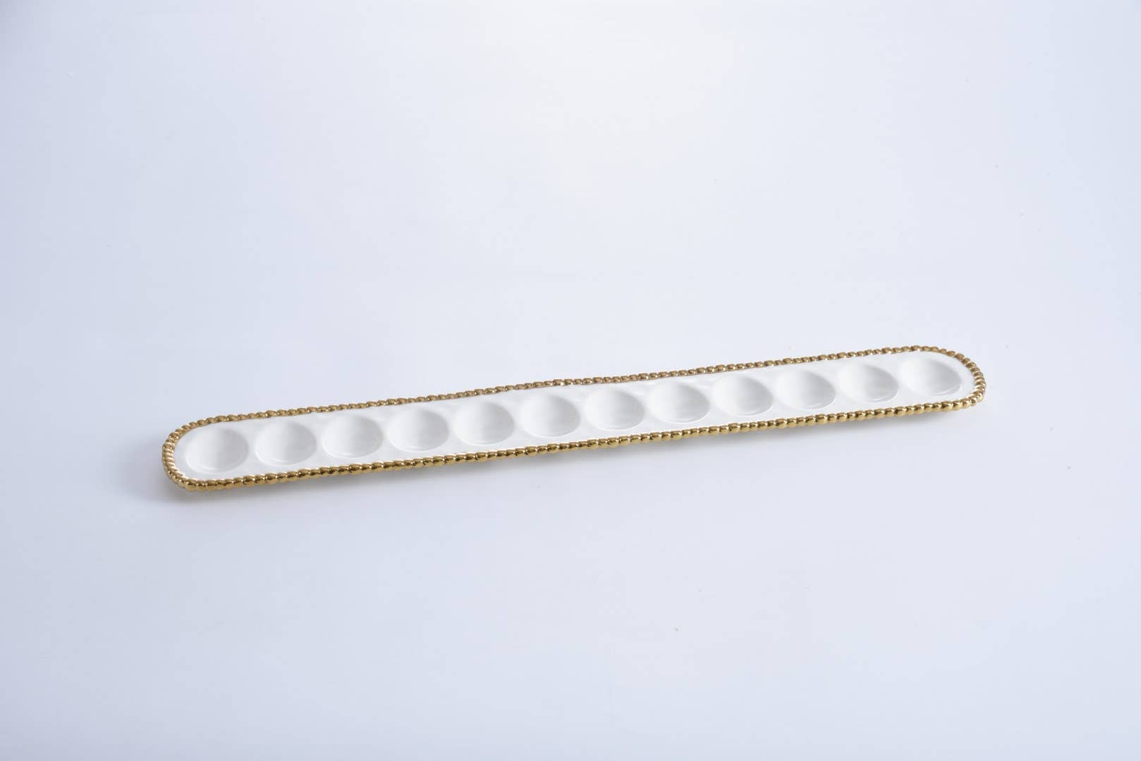 Long, narrow white dish with gold rim on a light gray background