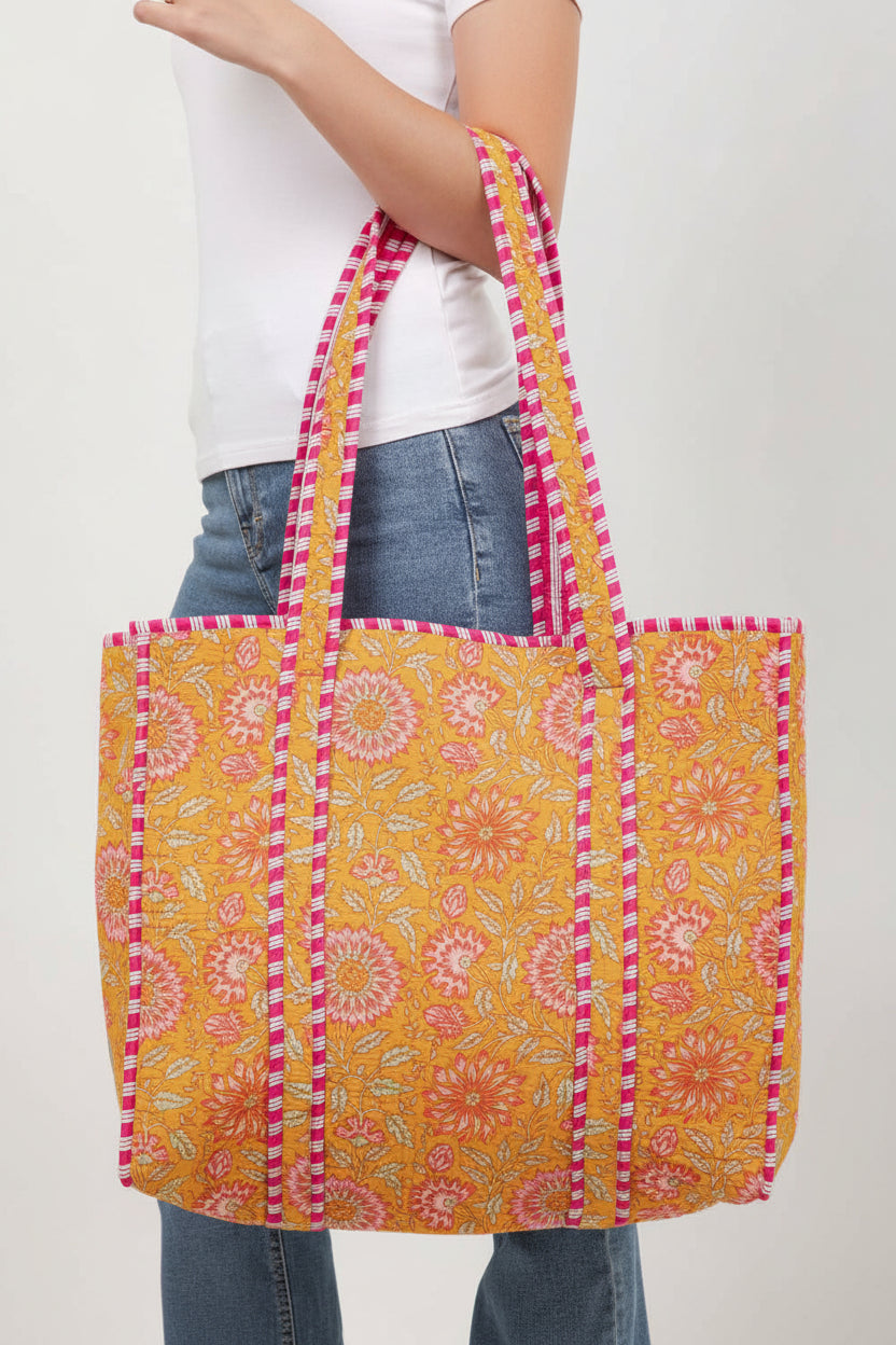 Person holding a colorful floral-patterned tote bag with pink and yellow accents.