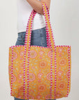 Person holding a colorful floral-patterned tote bag with pink and yellow accents.