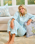 Woman in a blue patterned robe sitting on a couch with decorative pillows.