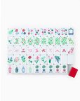 A set of Nantucket Tiles in red, light blue, and kelly green colors with various patterns and designs, displayed on a white surface alongside a red dice/coin bag.